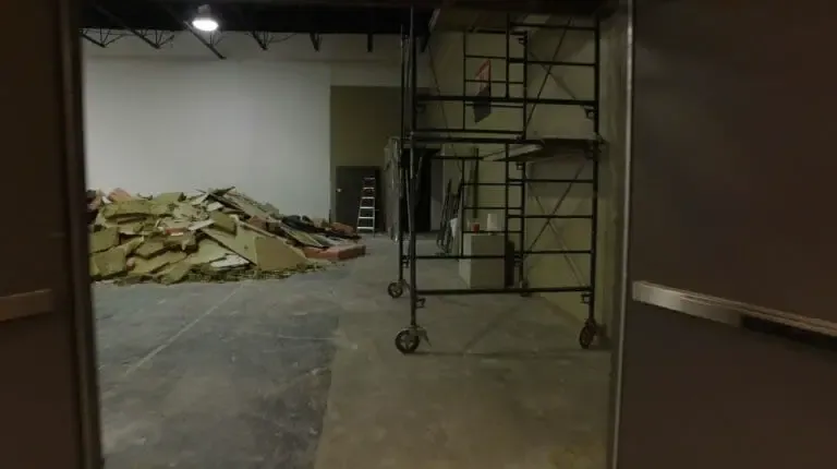 The corridor before, rubble piled on a bare concrete floor beside a rolling scaffold