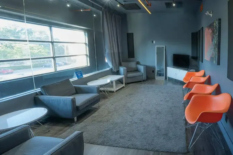 The green room after, sofas, a rug and orange chairs by the windows