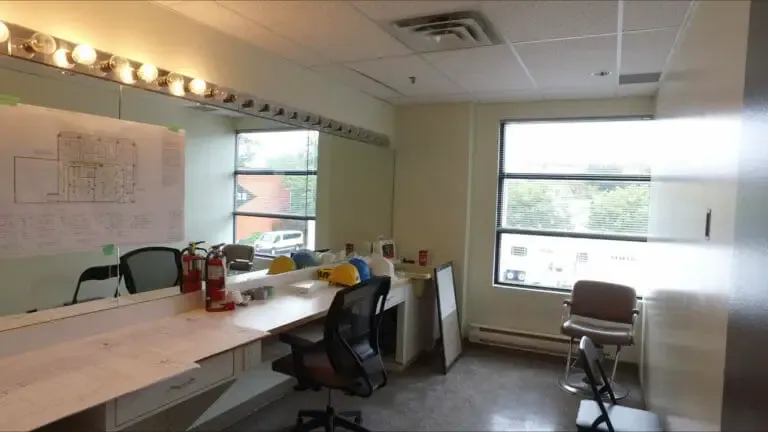 The hair and makeup room before, in use as an office with desks and a whiteboard