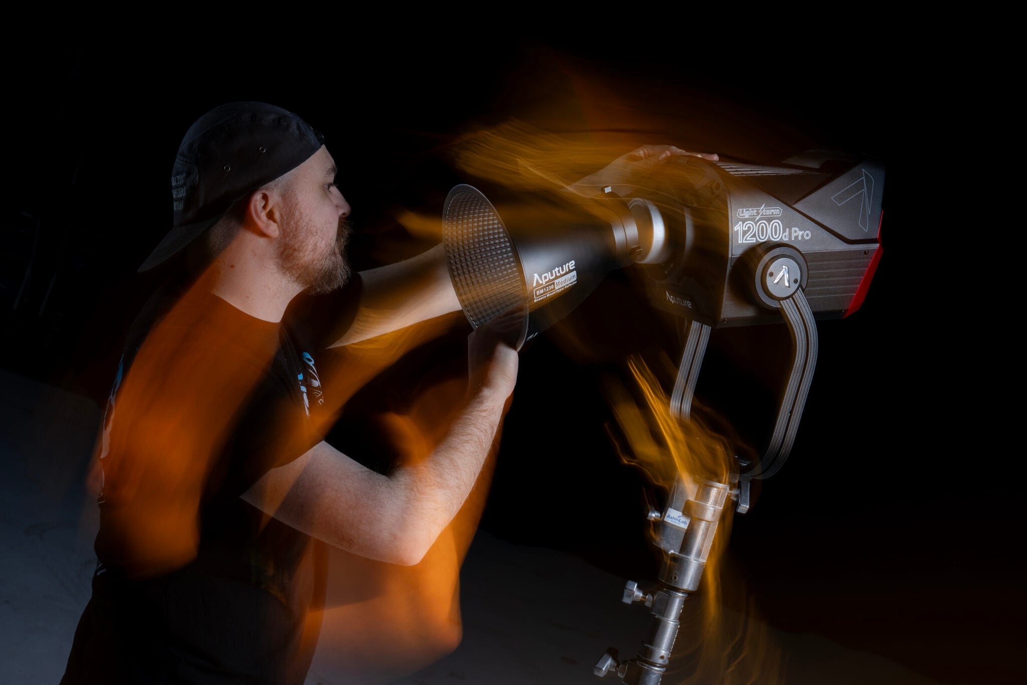 Jesse Kellestine adjusts an Aputure LS 1200d Pro on its stand in the dark studio, the light trailing orange in a long exposure