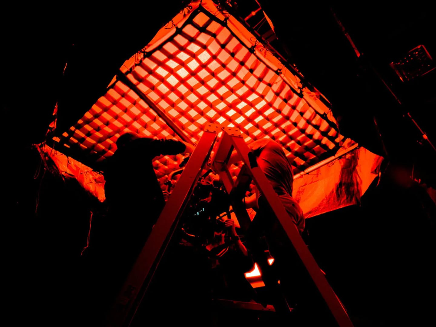 A crew member silhouetted behind a lattice frame under deep red light