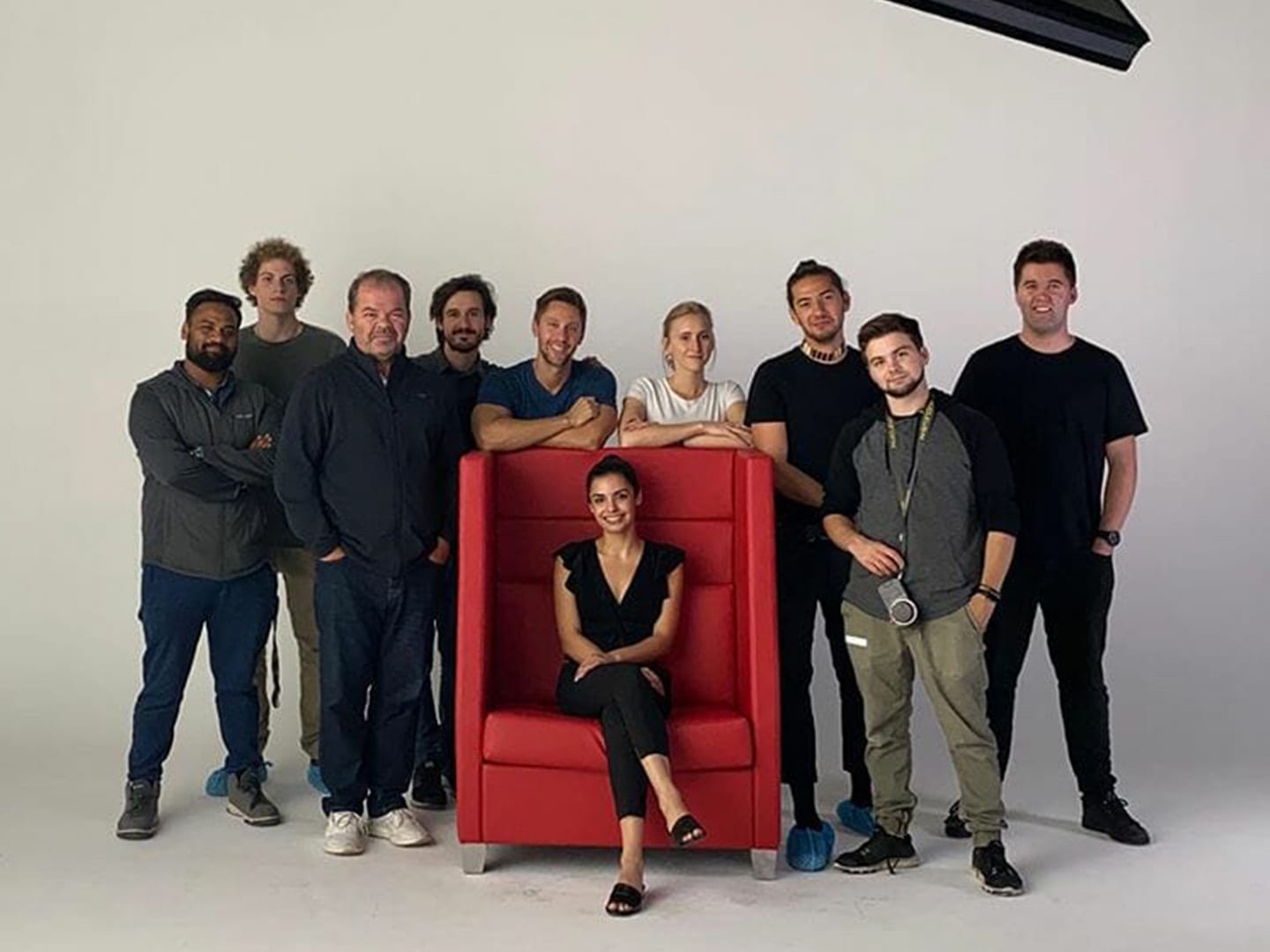 A dozen crew gathered around a red wingback chair on the white cyc