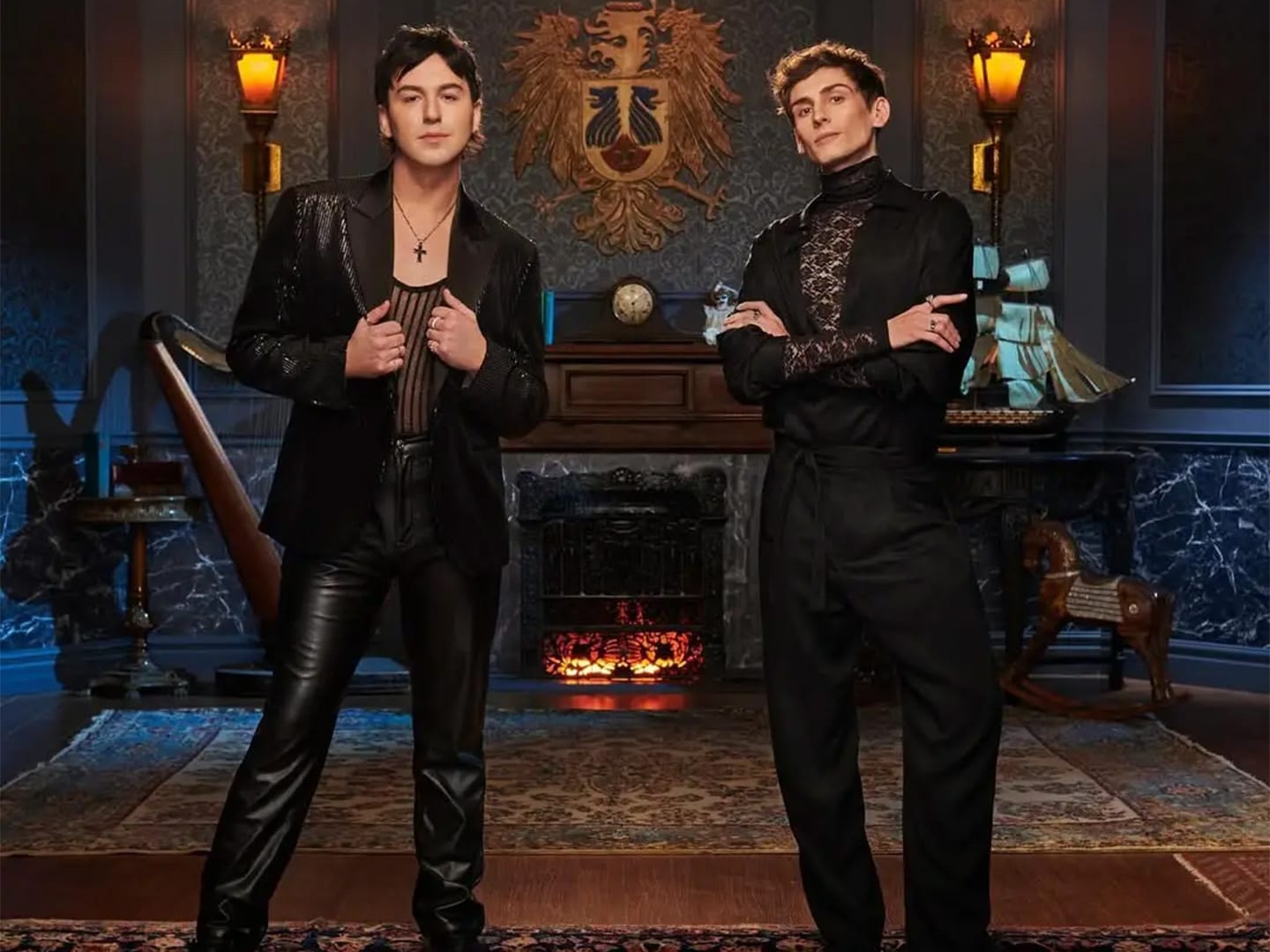 Two performers in black in front of a fireplace on a gothic interior build