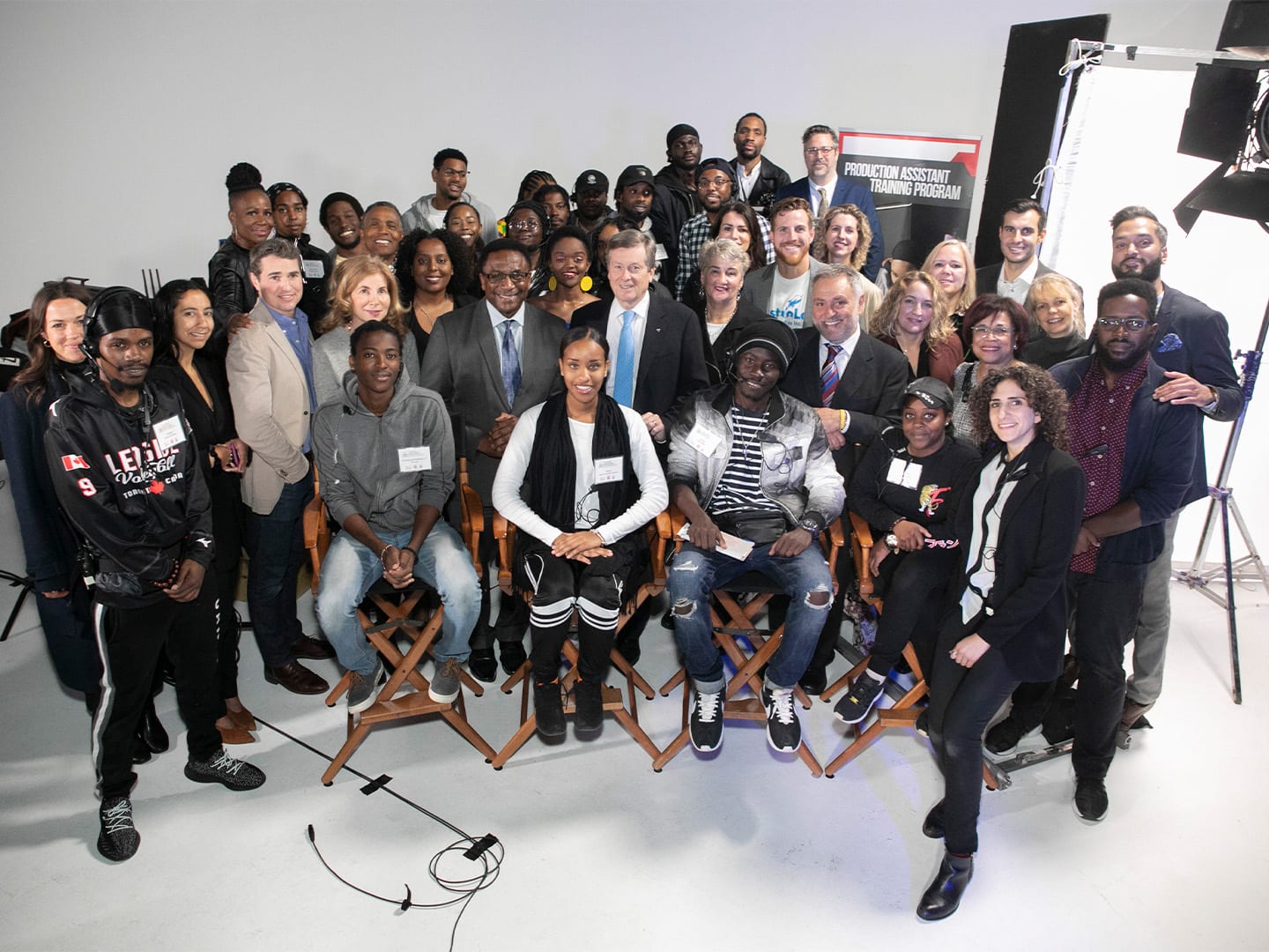 A crowd of guests and crew arranged across the white cyc for a group portrait, a lighting stand at the edge of frame