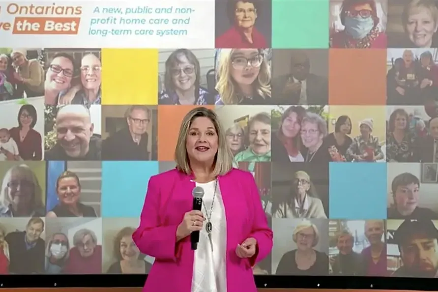 A speaker live streaming an announcement from the stage, in front of a wall of portraits