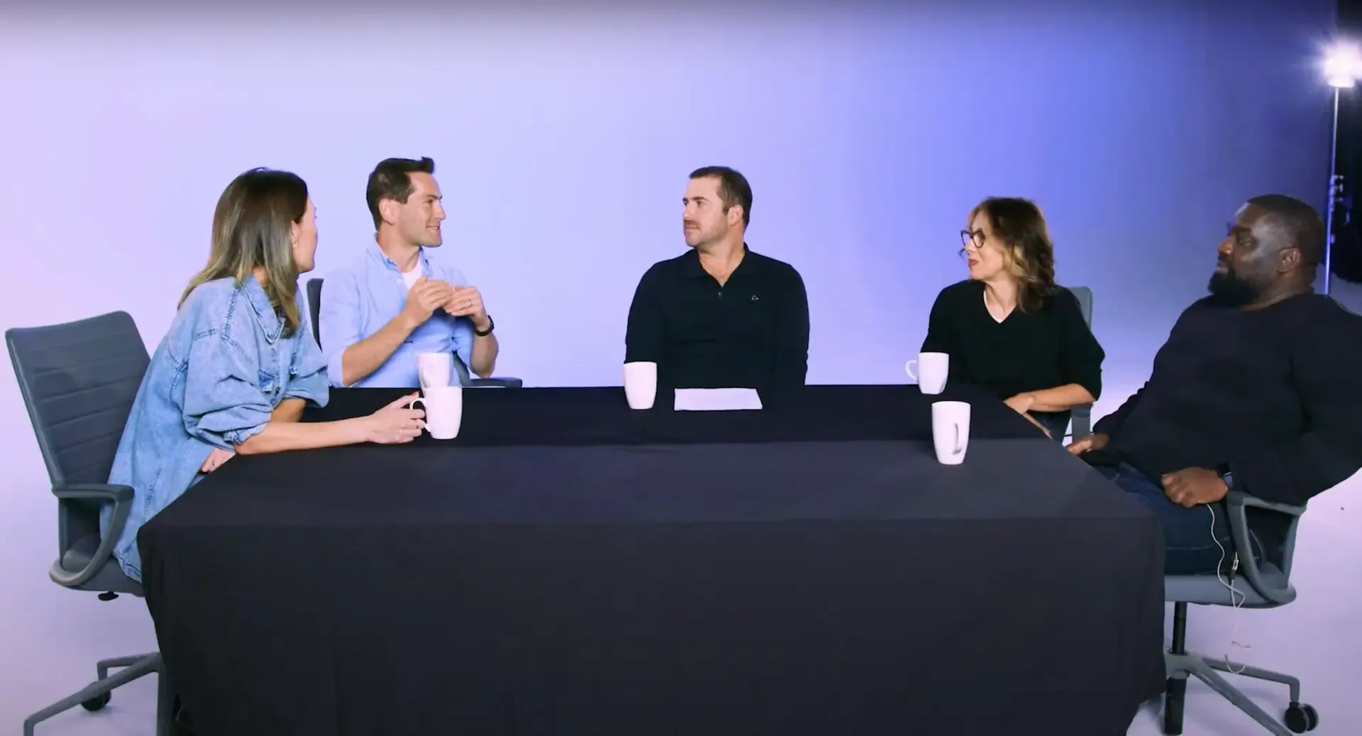 Five panelists in conversation at a table lit on the cyc