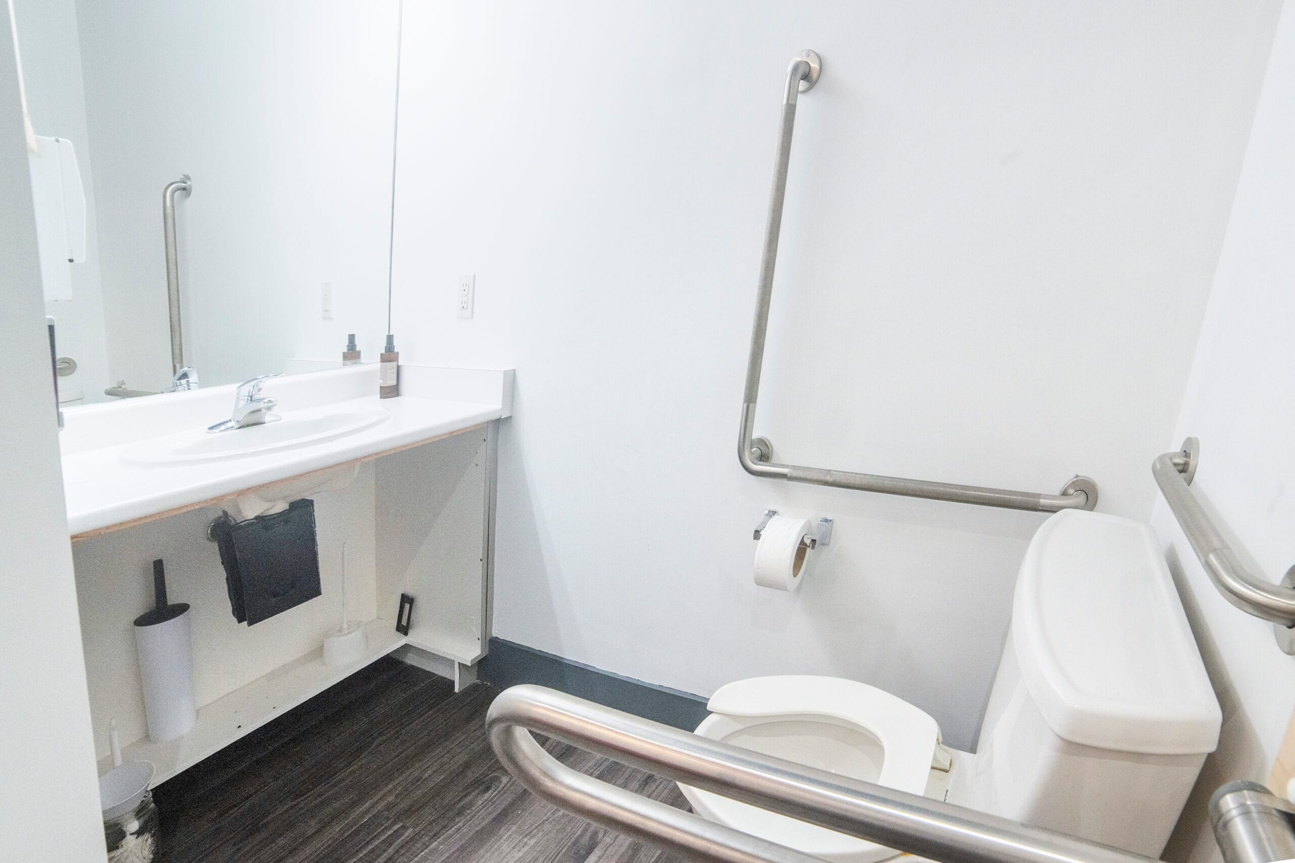 The accessible restroom, with grab bars beside and behind the toilet, a sink and a mirror