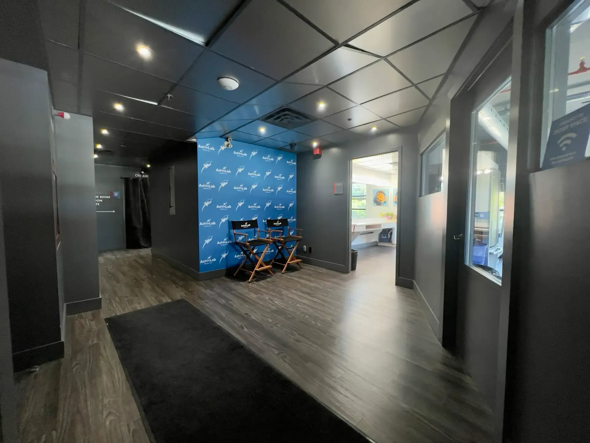 The entrance hall: a wide corridor with a dark floor, a blue AstroLab backdrop with two director's chairs, and an open doorway to a room on the right