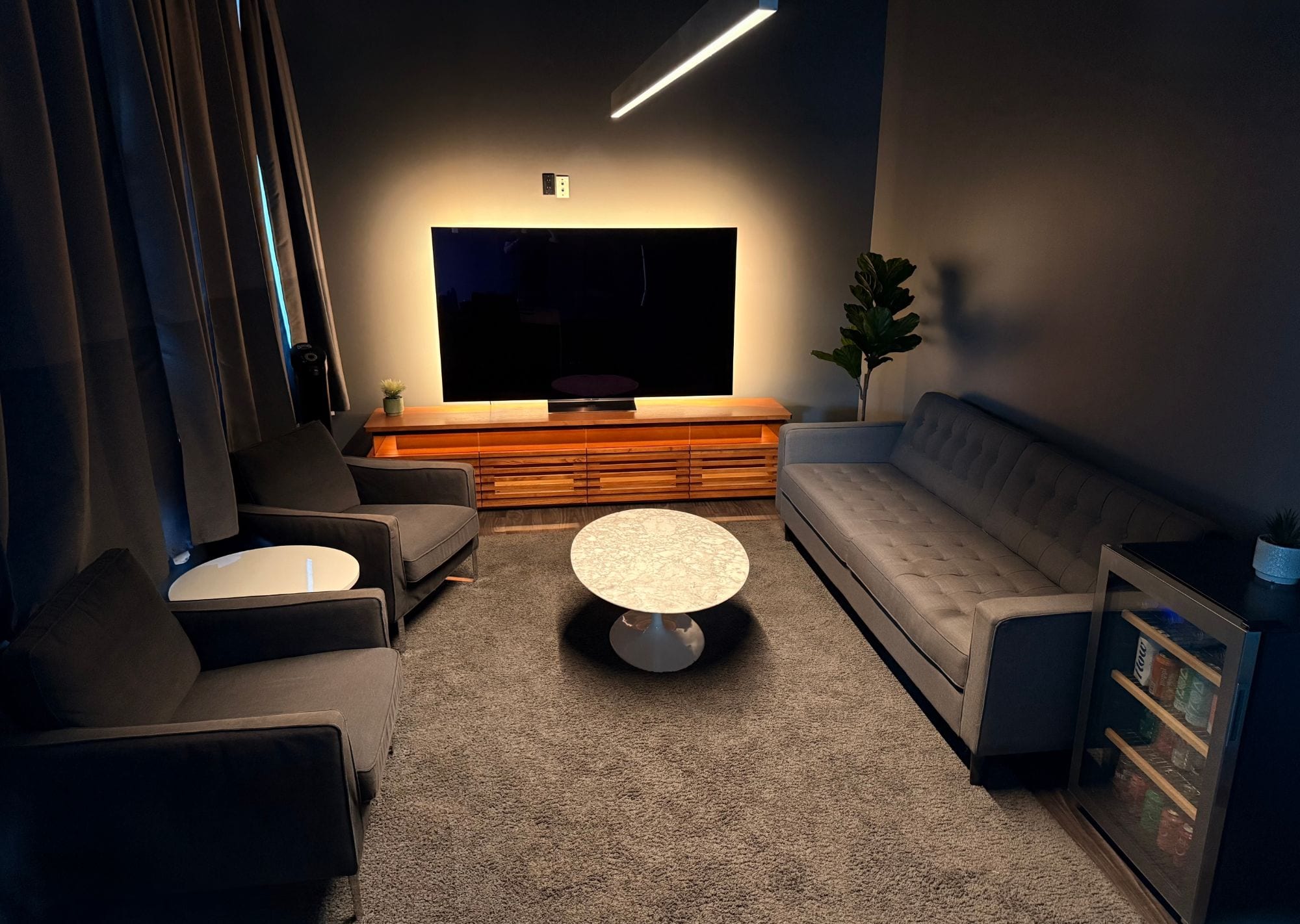 The green room, a tufted sofa and two armchairs round a marble coffee table, facing a backlit TV