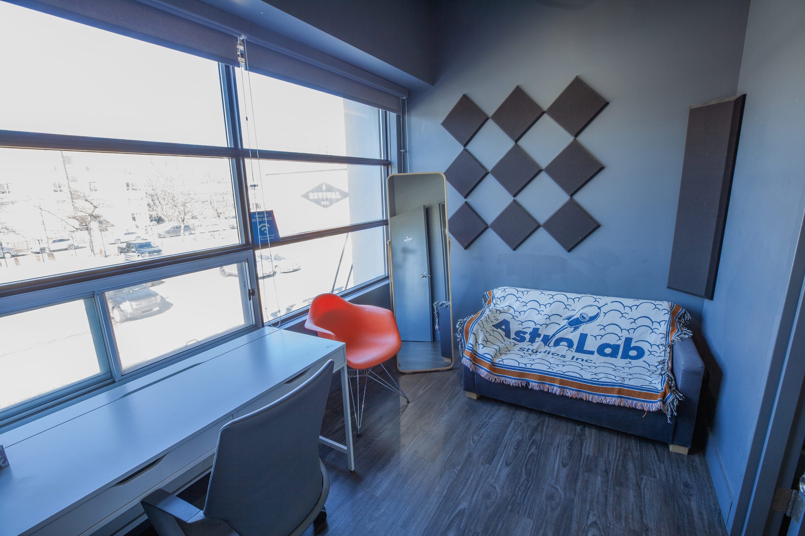The private office, a desk along the windows and a sofa under acoustic panels